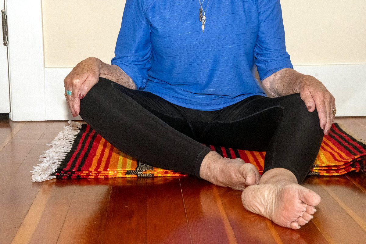 Seated floor movement — crossed legs and relaxed feet on a woven mat