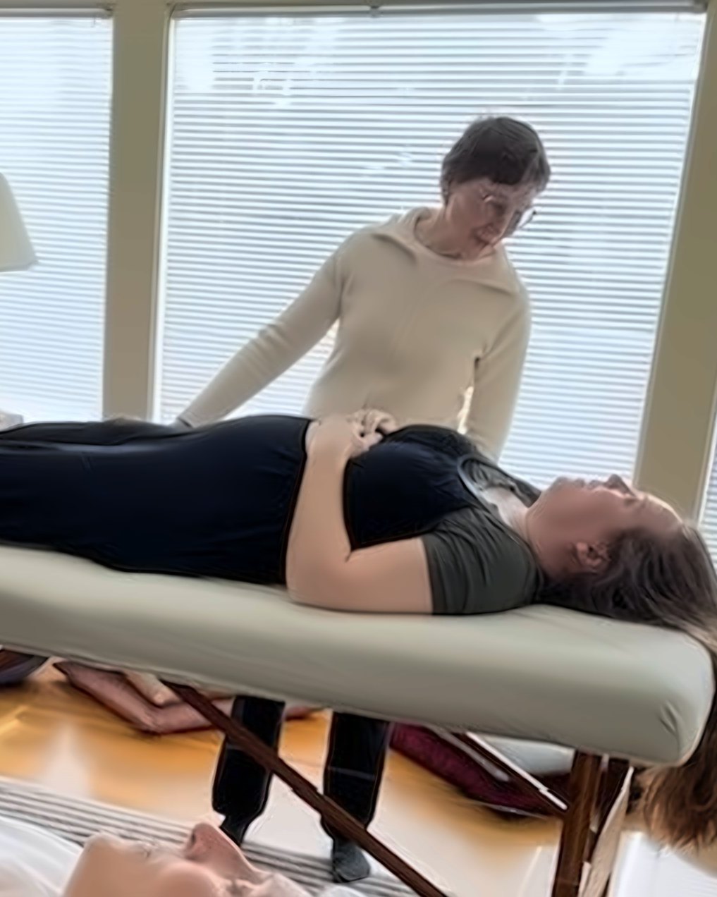 Linda Eisenman giving a Trager® Touch bodywork session at the table, by a window full of light